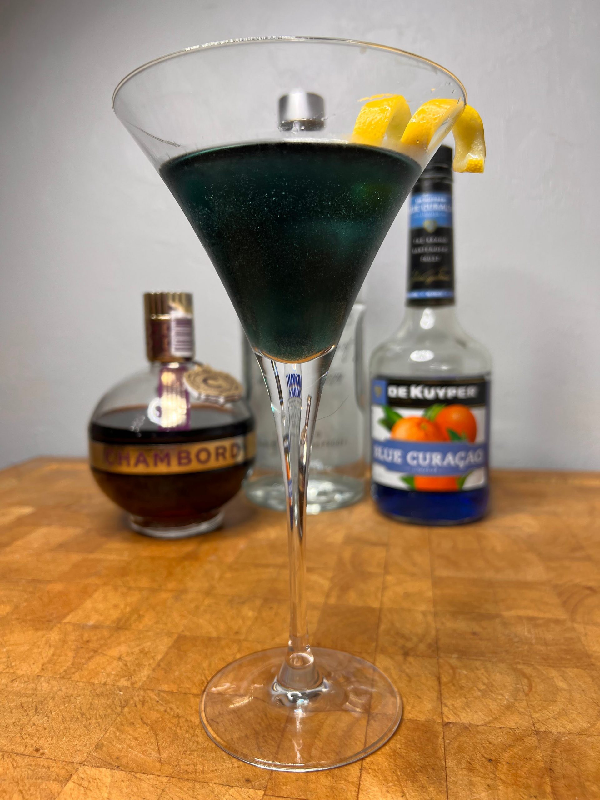 close up of black martini with liquor bottles visible in the background