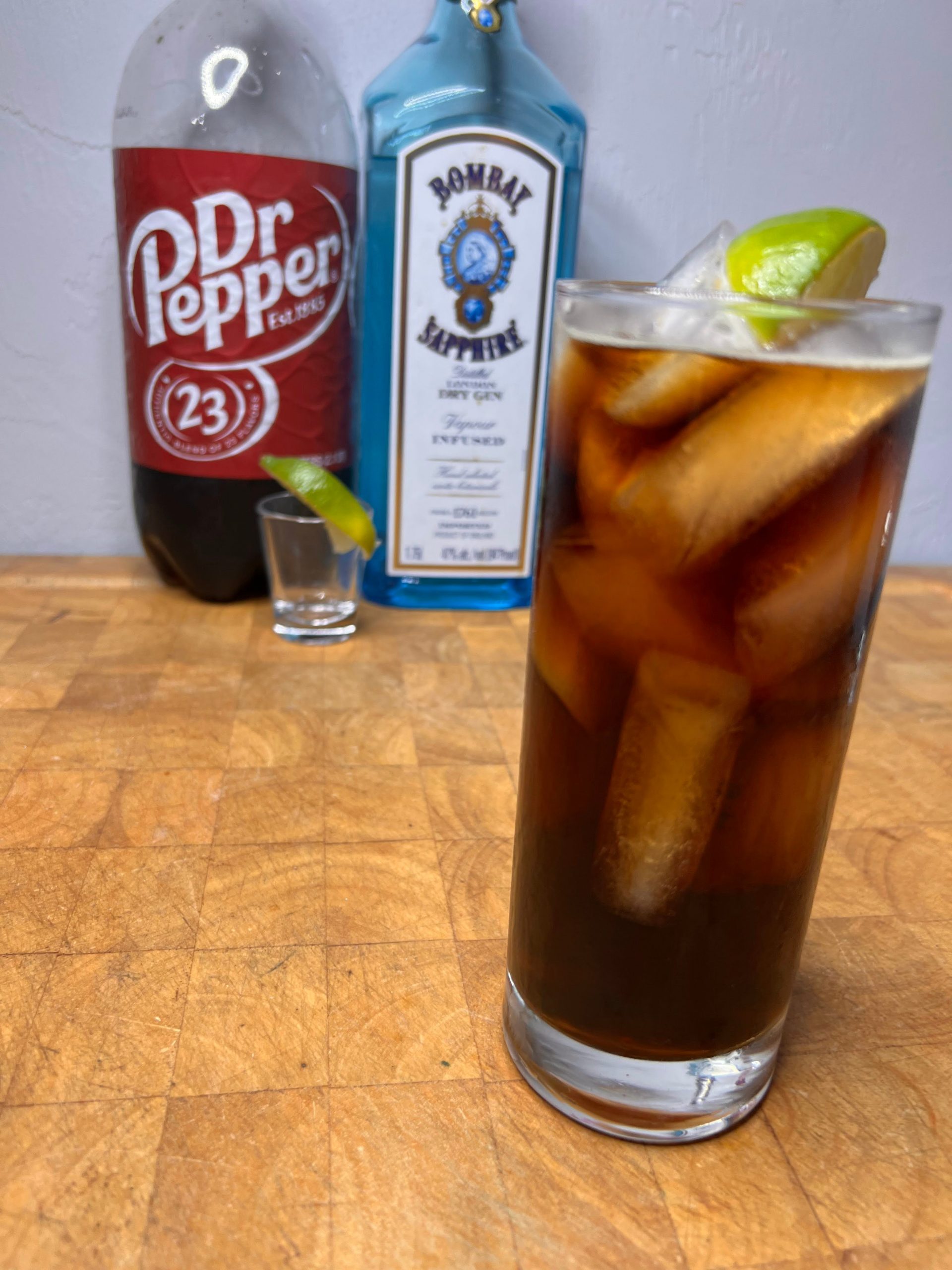 gin and dr pepper in glass with bottles in background