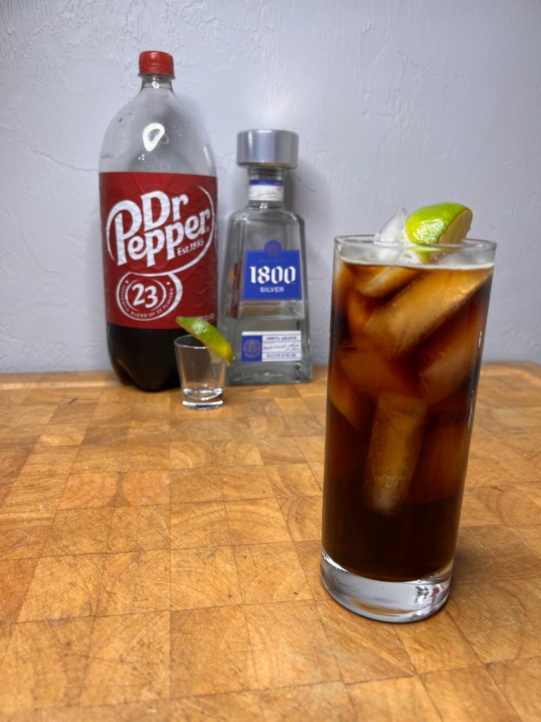 close up of dr pepper & tequila with liquor bottles visible in the background