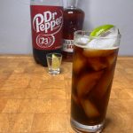 glass of whiskey and dr pepper with bottles in background