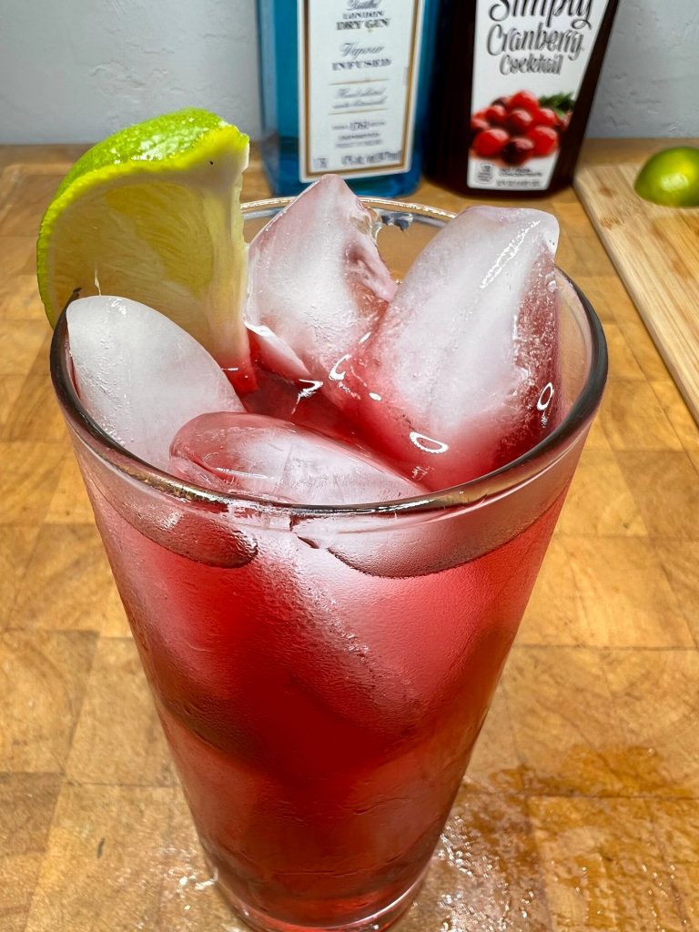 close up of gin and cranberry with liquor bottles visible in the background