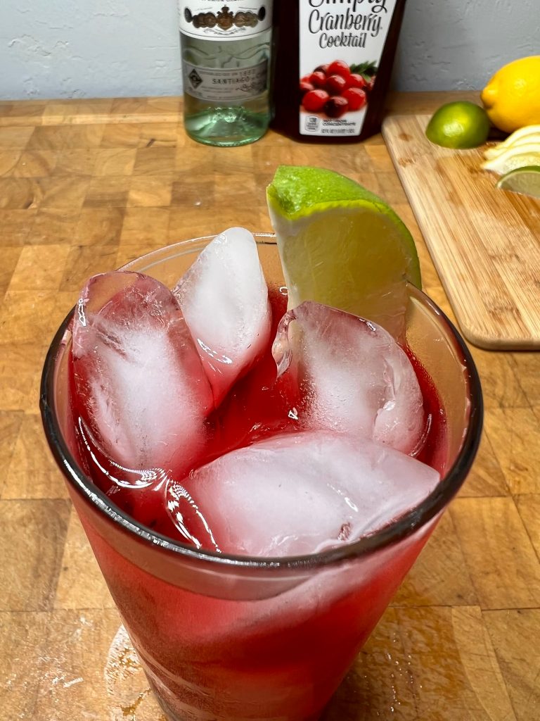 close up of rum and cranberry with liquor bottles visible in the background