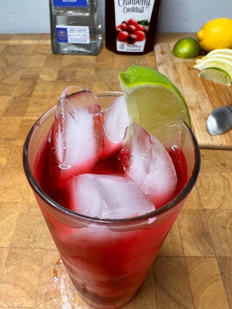 close up of tequila & cranberry with liquor bottles visible in the background
