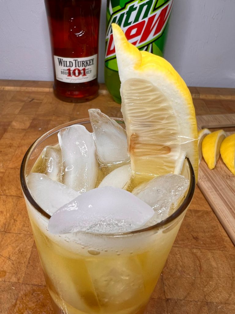 close up of whiskey & mountain dew with liquor bottles visible in the background