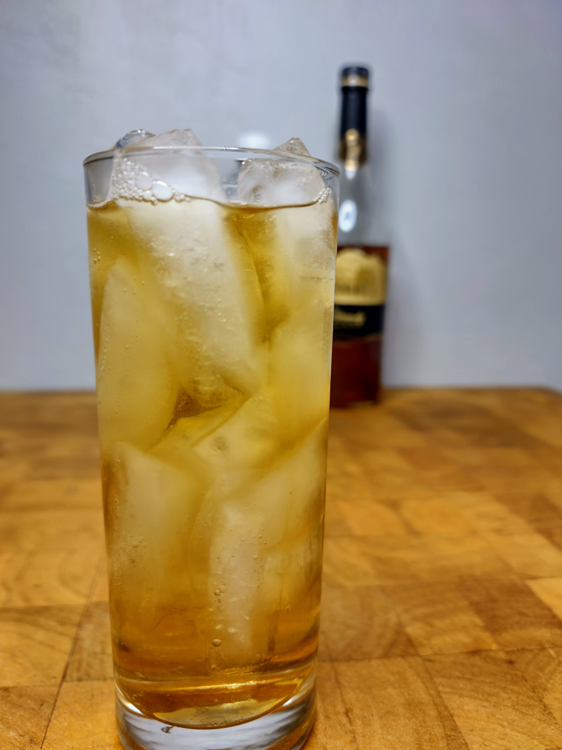 closeup of brandy and tonic in a highball glass with bottle of brandy in the background
