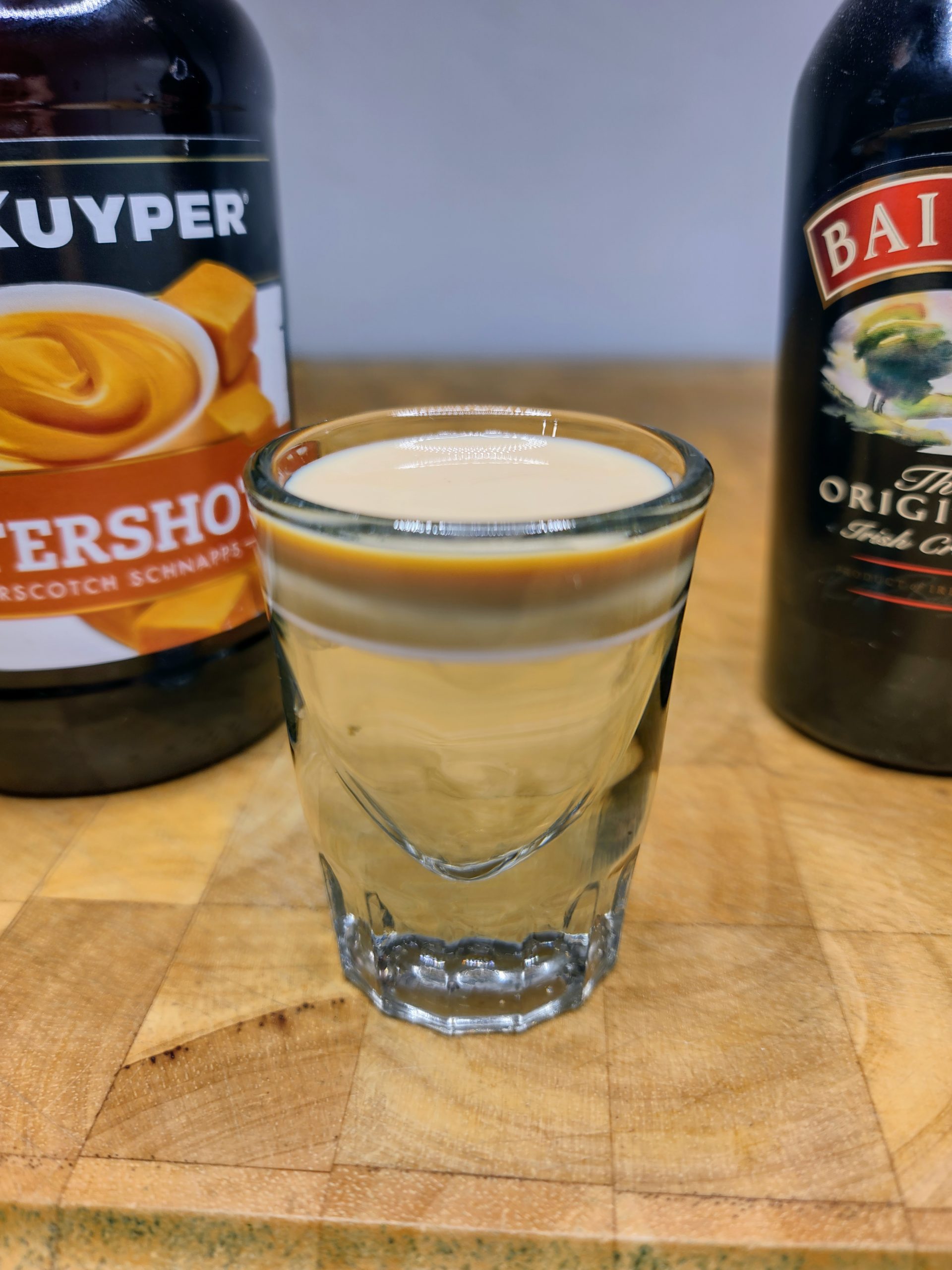 buttery nipple shot with ingredient bottles behind the drink