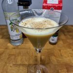 eggnog martini with nutmeg on top and ingredients behind the glass