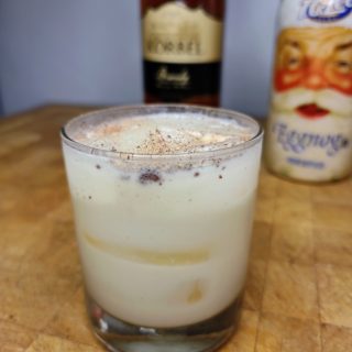 closeup of brandy and eggnog with nutmeg on top of drink on wooden table