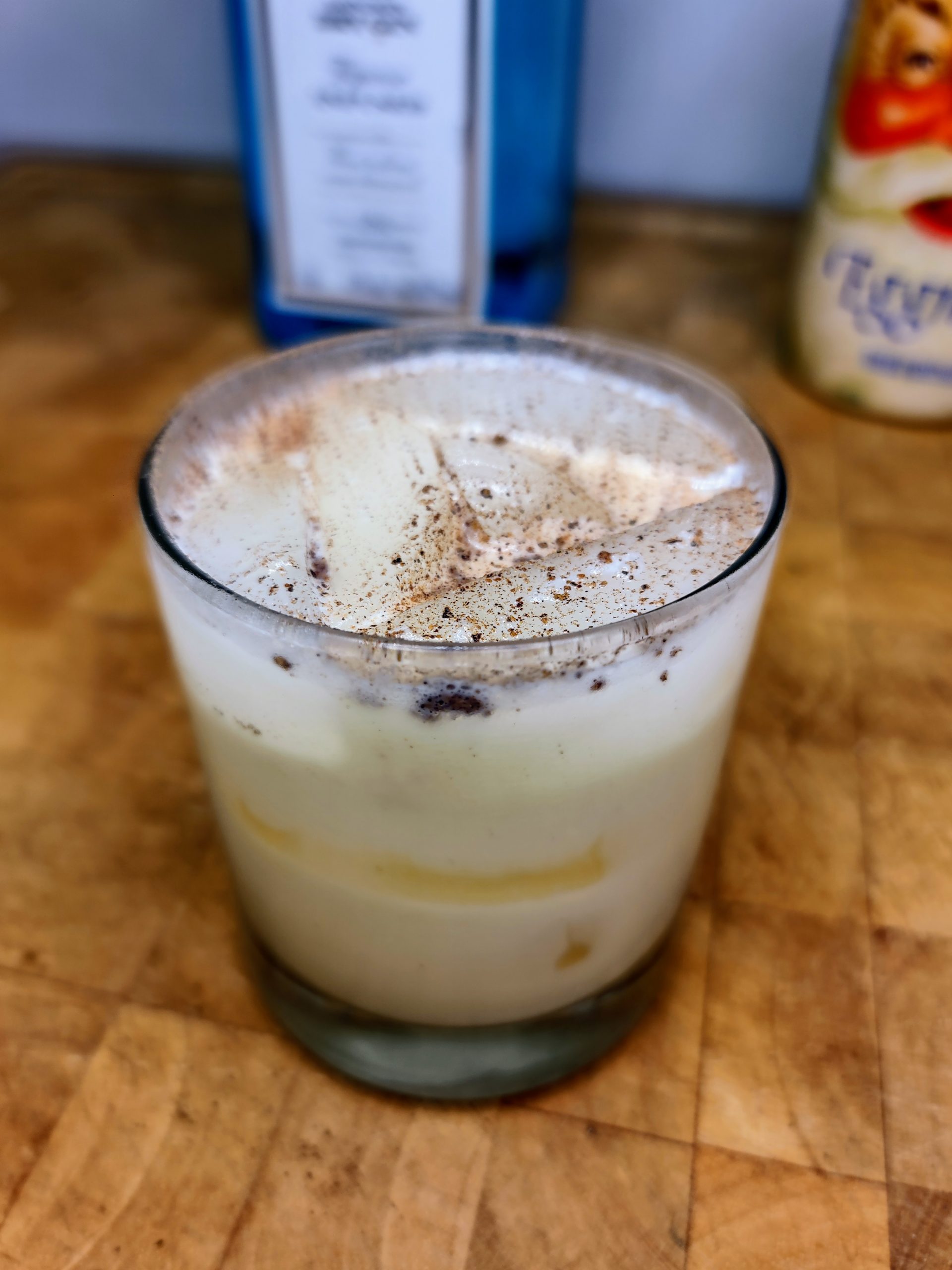 closeup of gin and eggnog with nutmeg on top on a wooden table