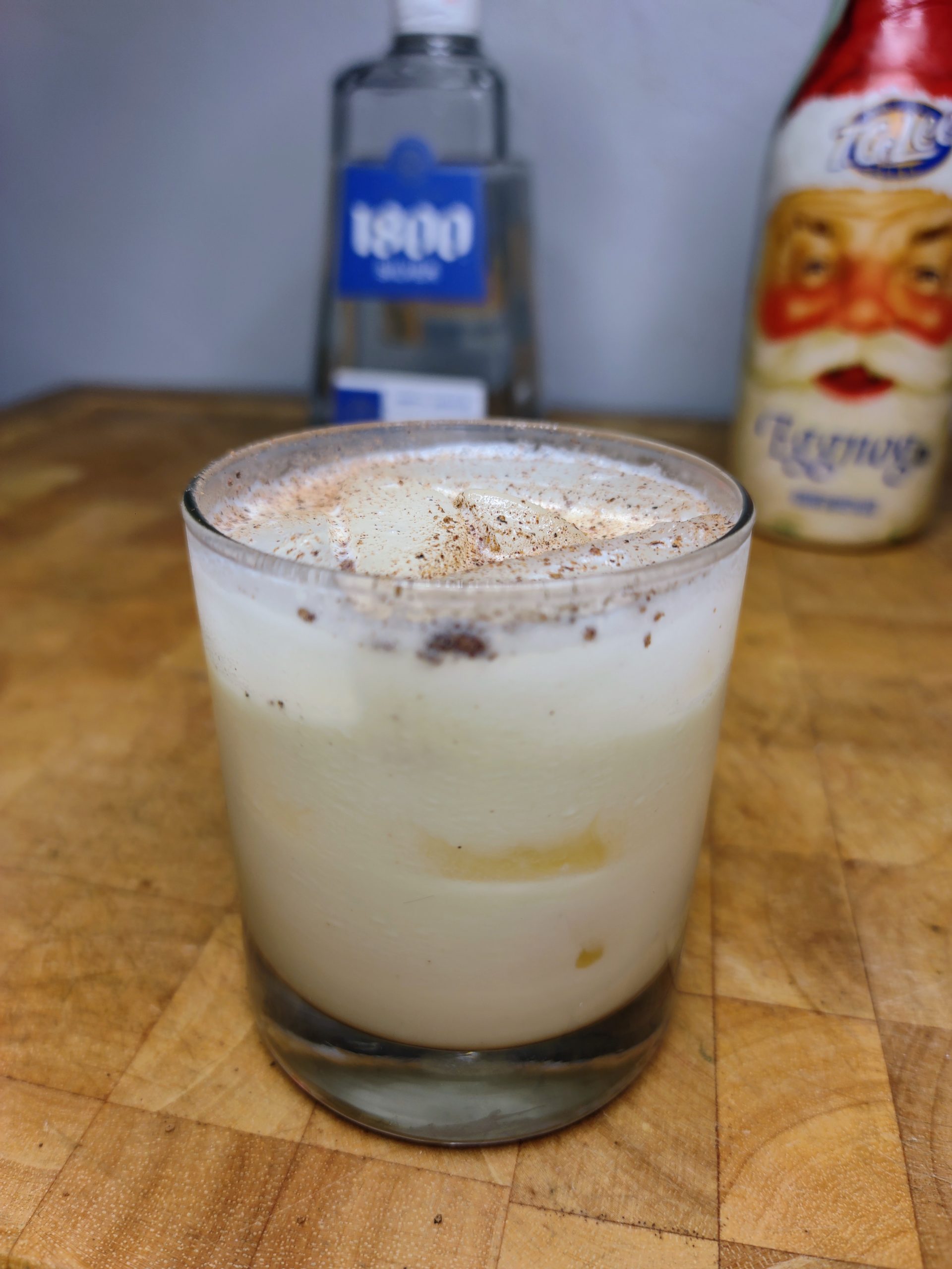closeup of tequila and eggnog with nutmeg on top on a wooden table
