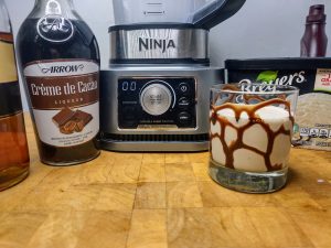 frozen brandy alexander in a rocks glass next to blender and other ingredients