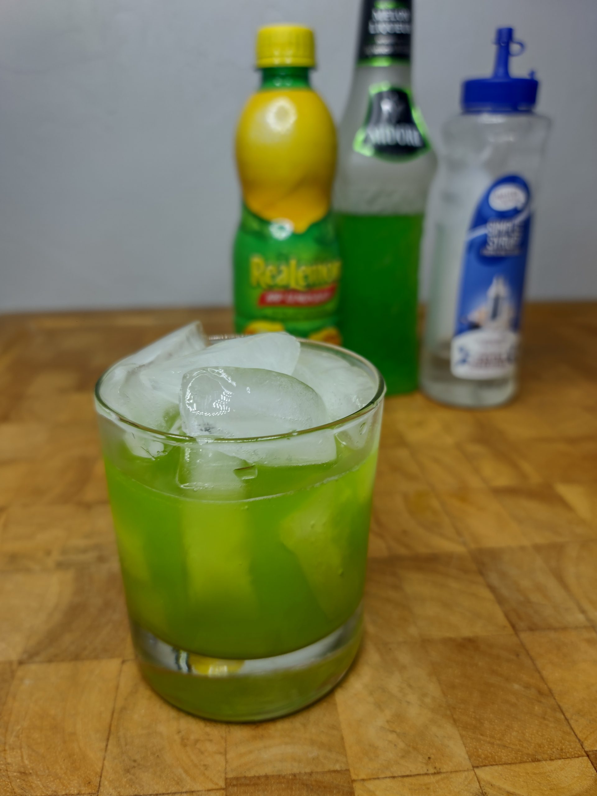 midori sour in rocks glass with ingredient bottles in the background