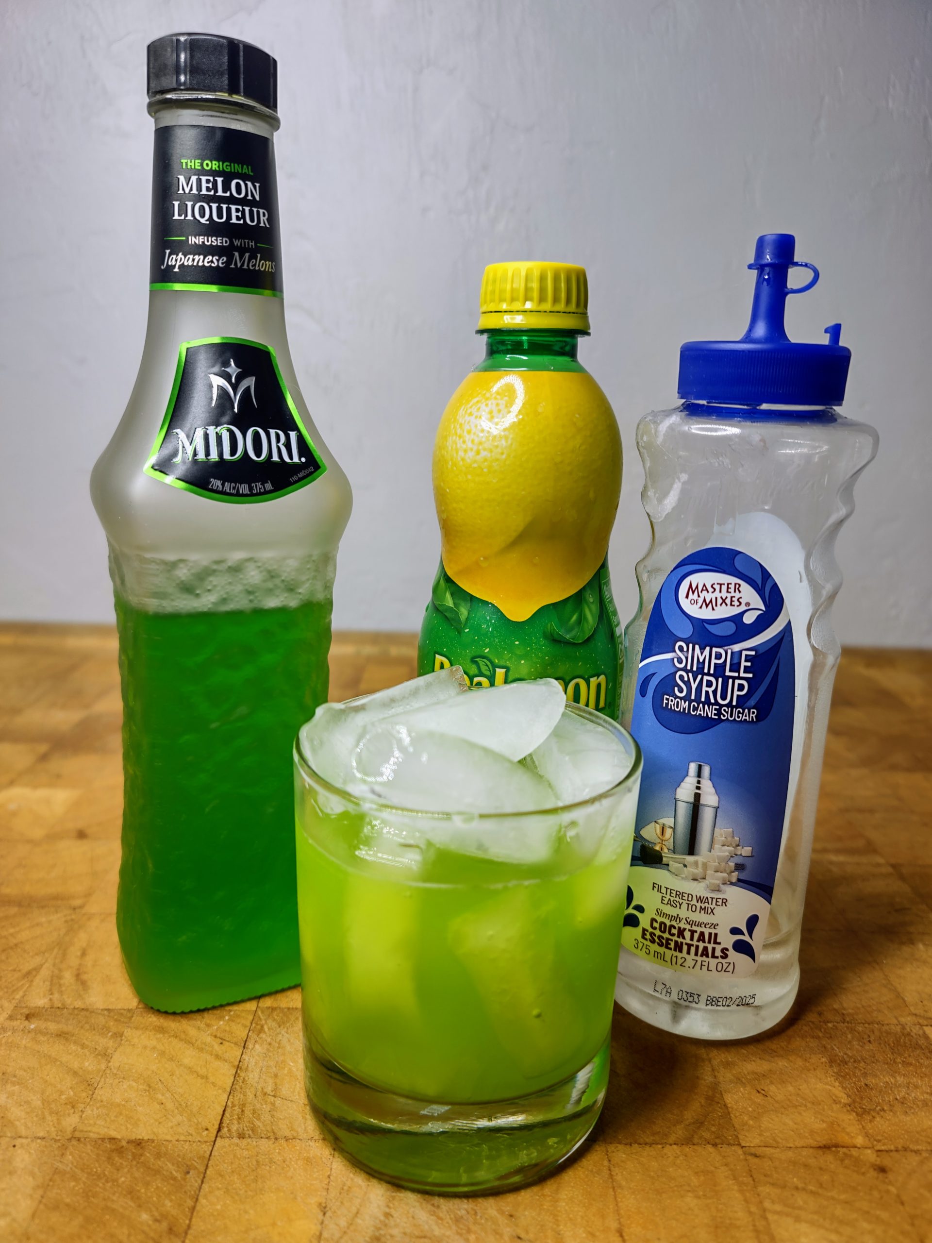 midori sour with ingredients around the drink glass.