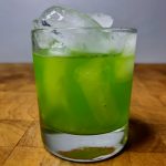 closeup of midori sour in a rocks glass on a wooden table