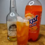 whiskey and orange soda in a highball glass with ingredients behind the drink