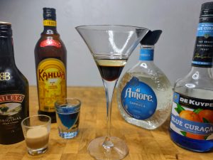 martini glass with layered kahlua and sambuca next to shot glasses with blue curacao and irish cream