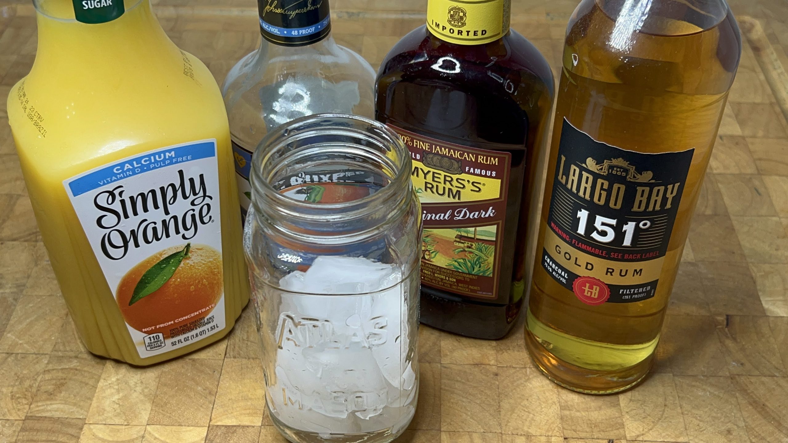 mason jar with ice next to bottles of 151 rum, dark rum, blue curacao and orange juice