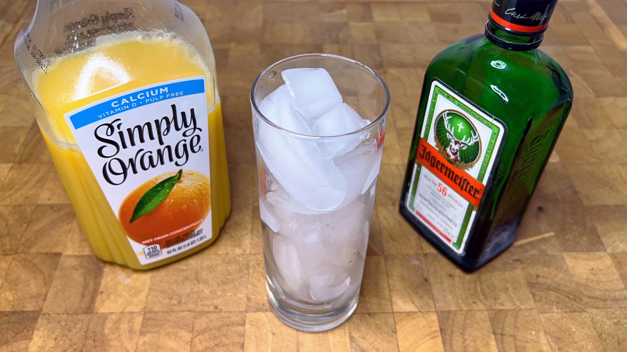 highball glass filled with ice with bottles of orange juice and jager next to the glass