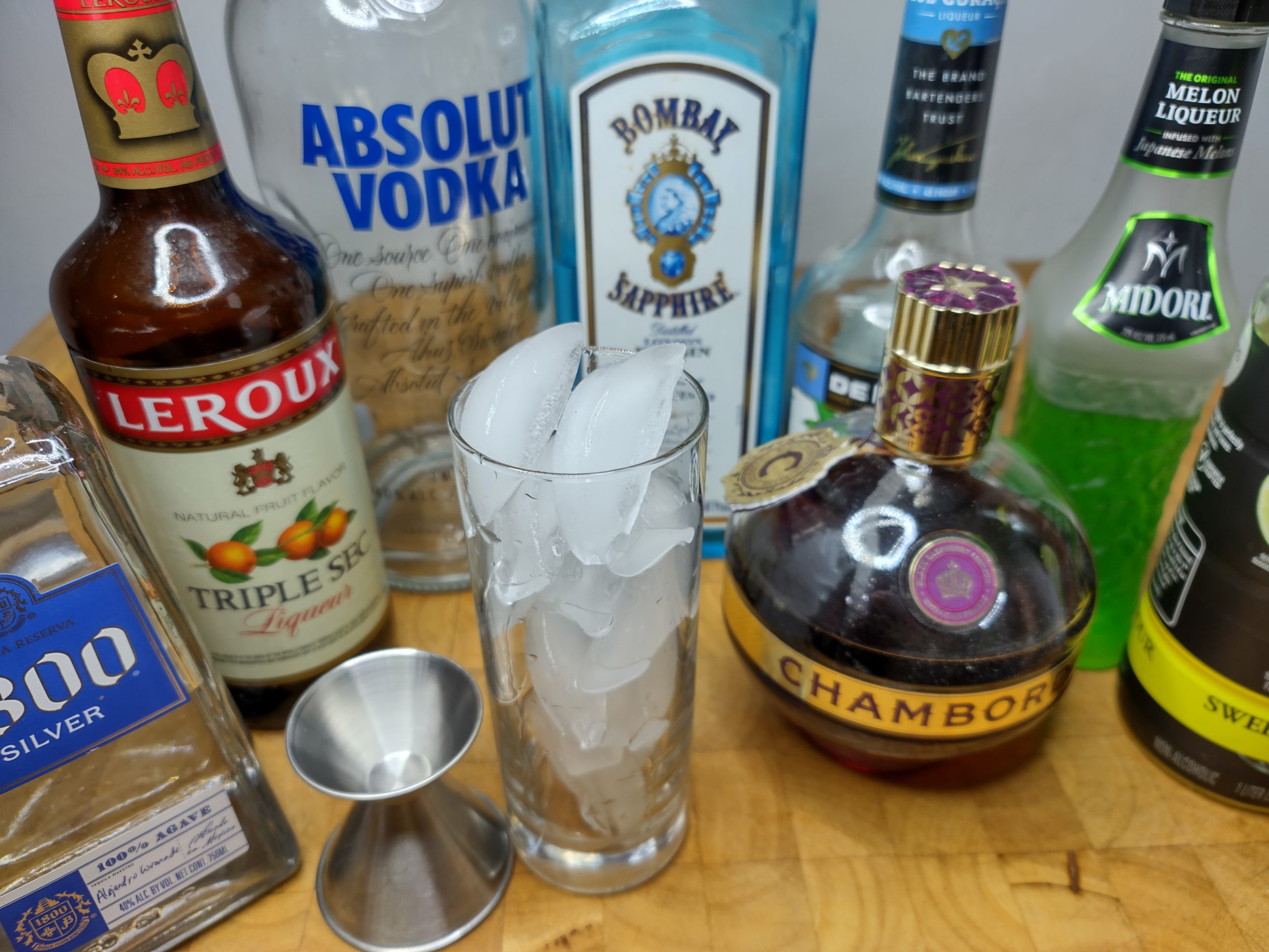 highball glass with ice next to a jigger and all the bottles of liquor used to make a la water cocktail