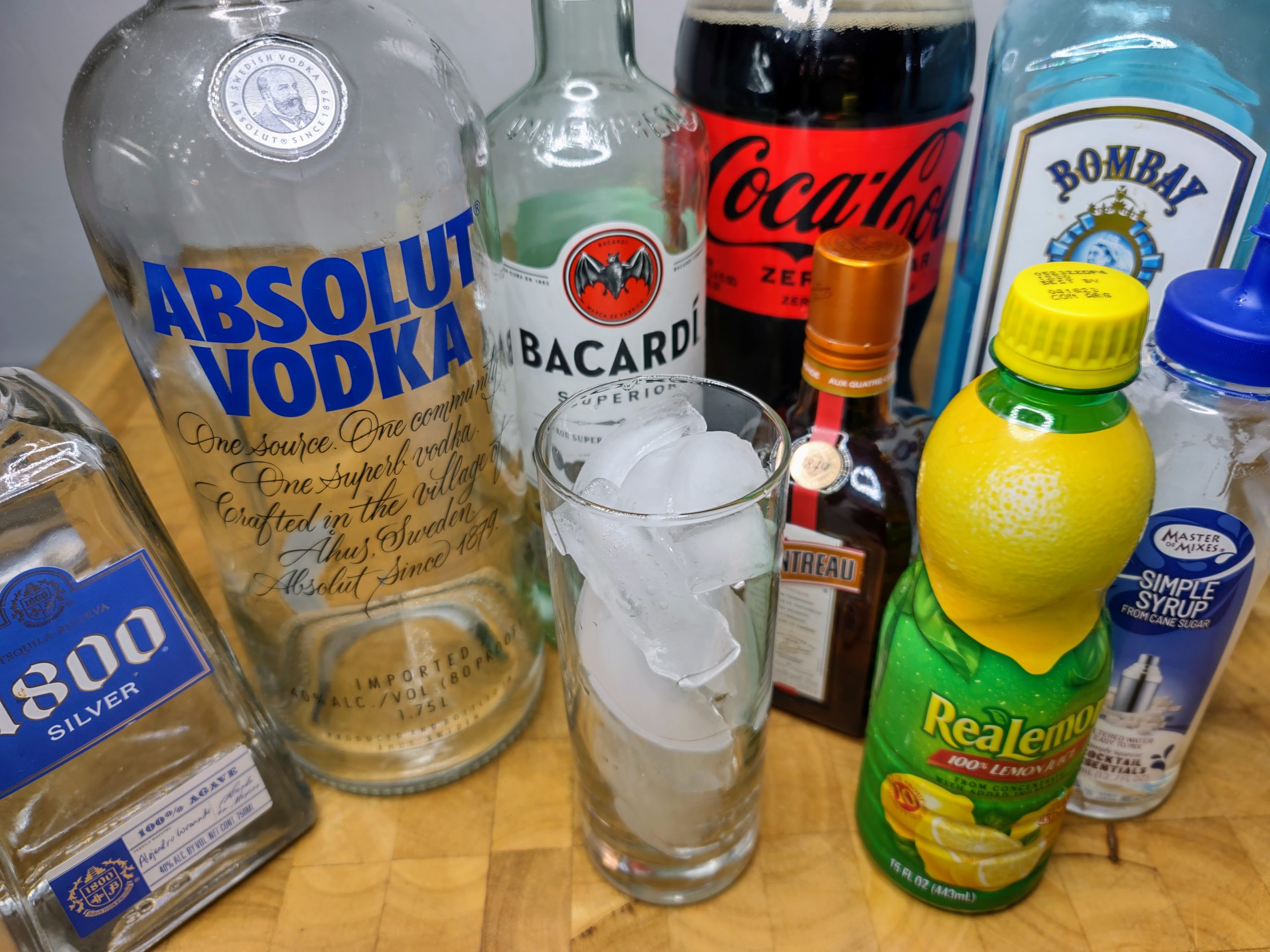 highball glass with ice next to all the ingredients needed for a long island iced tea