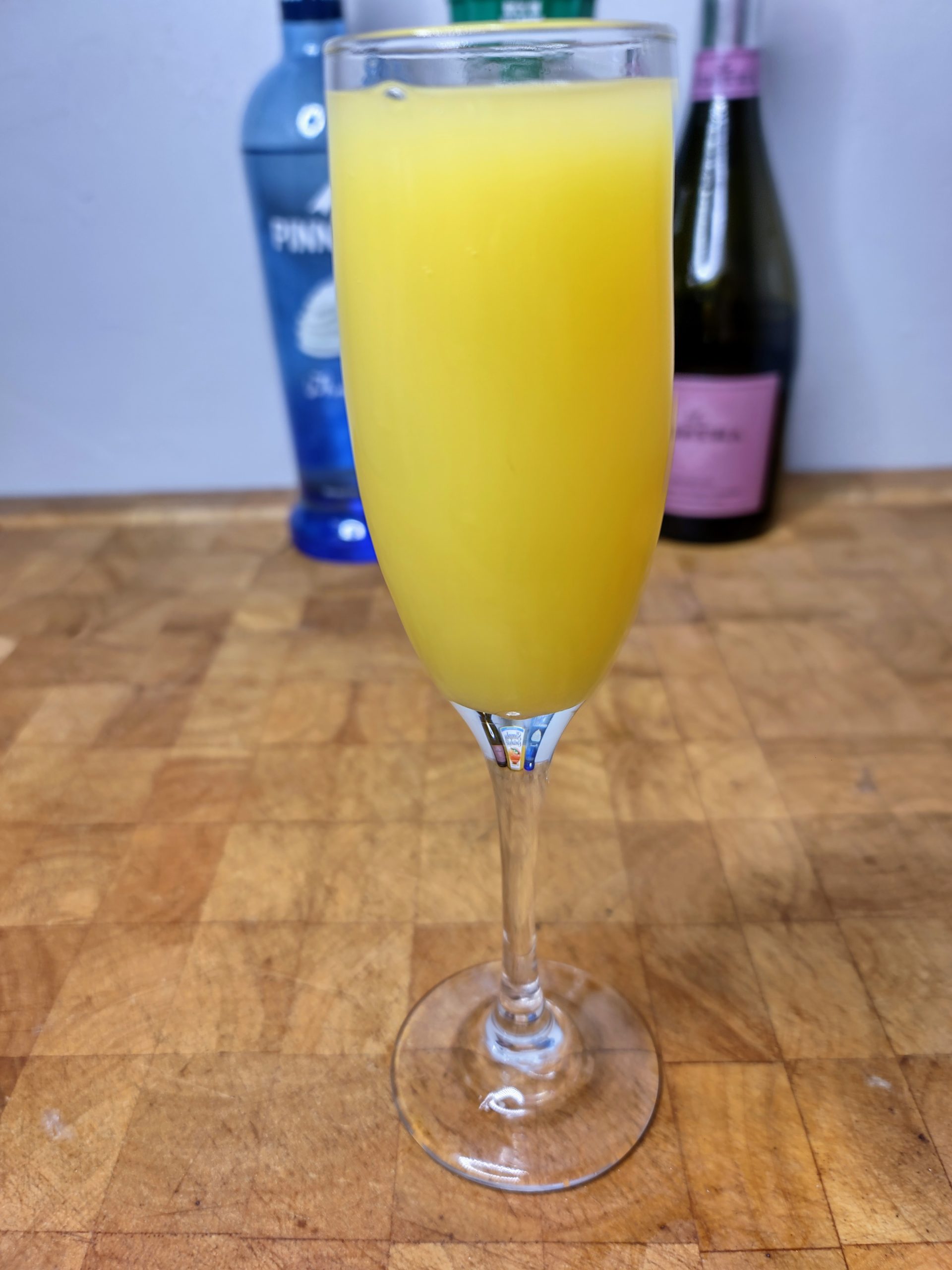 closeup of orange creamsicle mimosa with ingredients behind the glass