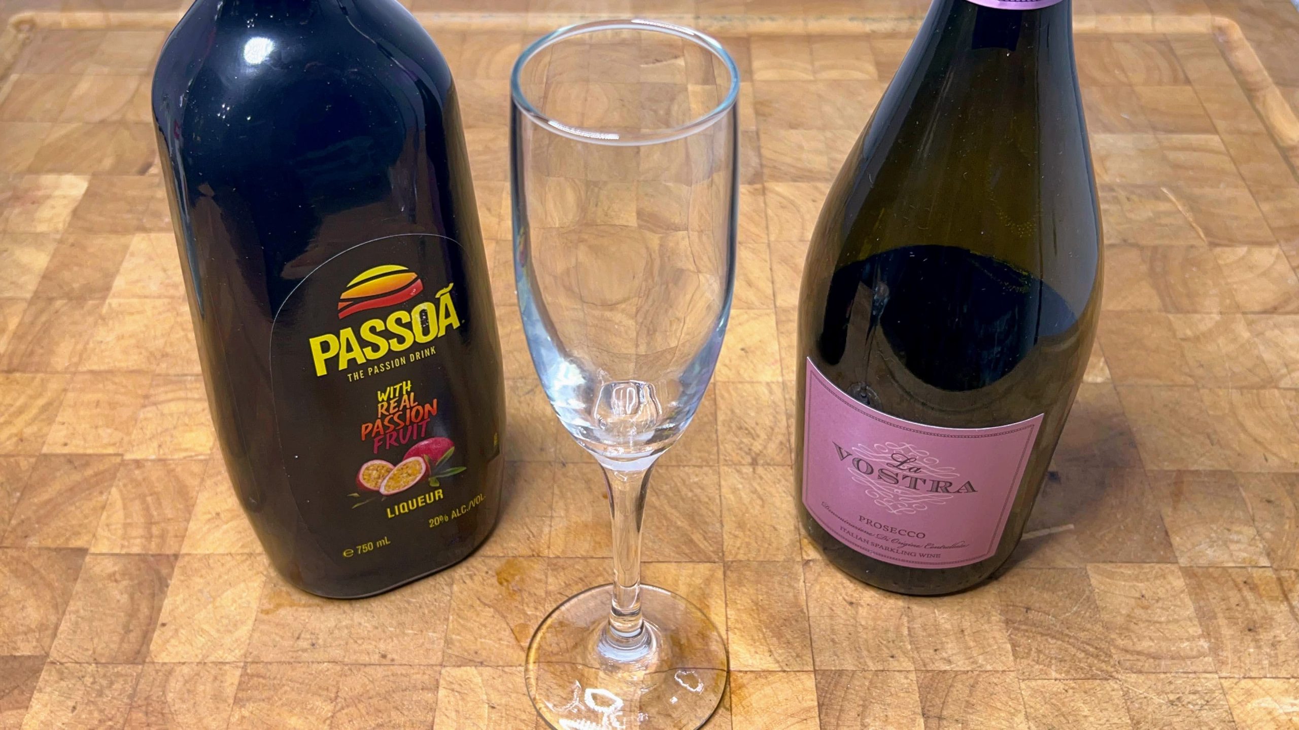 empty champagne flute with bottle of passoa and champagne next to it