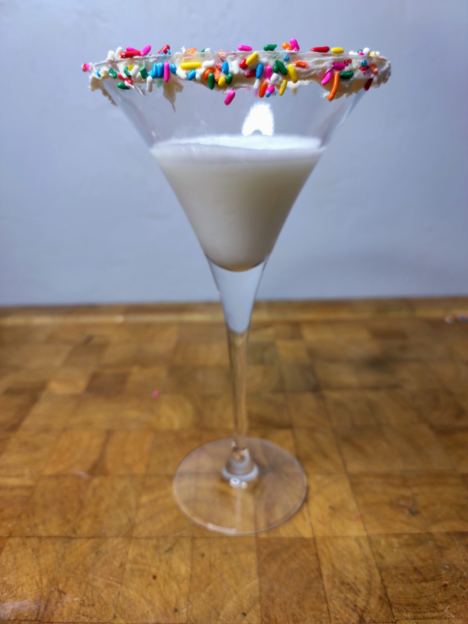 closeup of a birthday cake martini with sprinkles on the glass rim.
