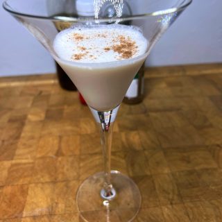 closeup of a brandy alexander drink in a martini glass with nutmeg on top.