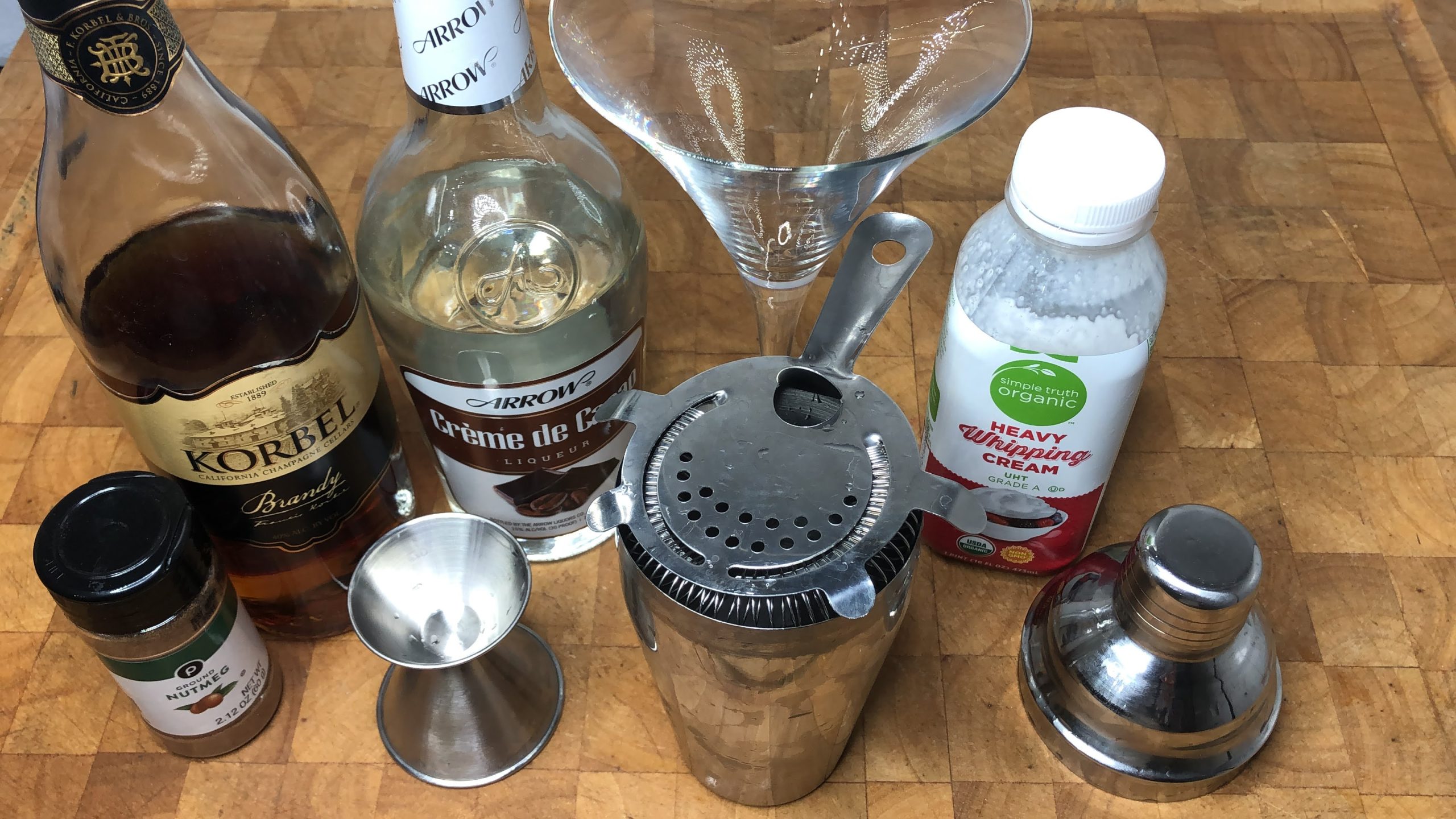empty martini glass next to a jigger, shaker, heavy cream, nutmeg, brandy and light creme de cacao
