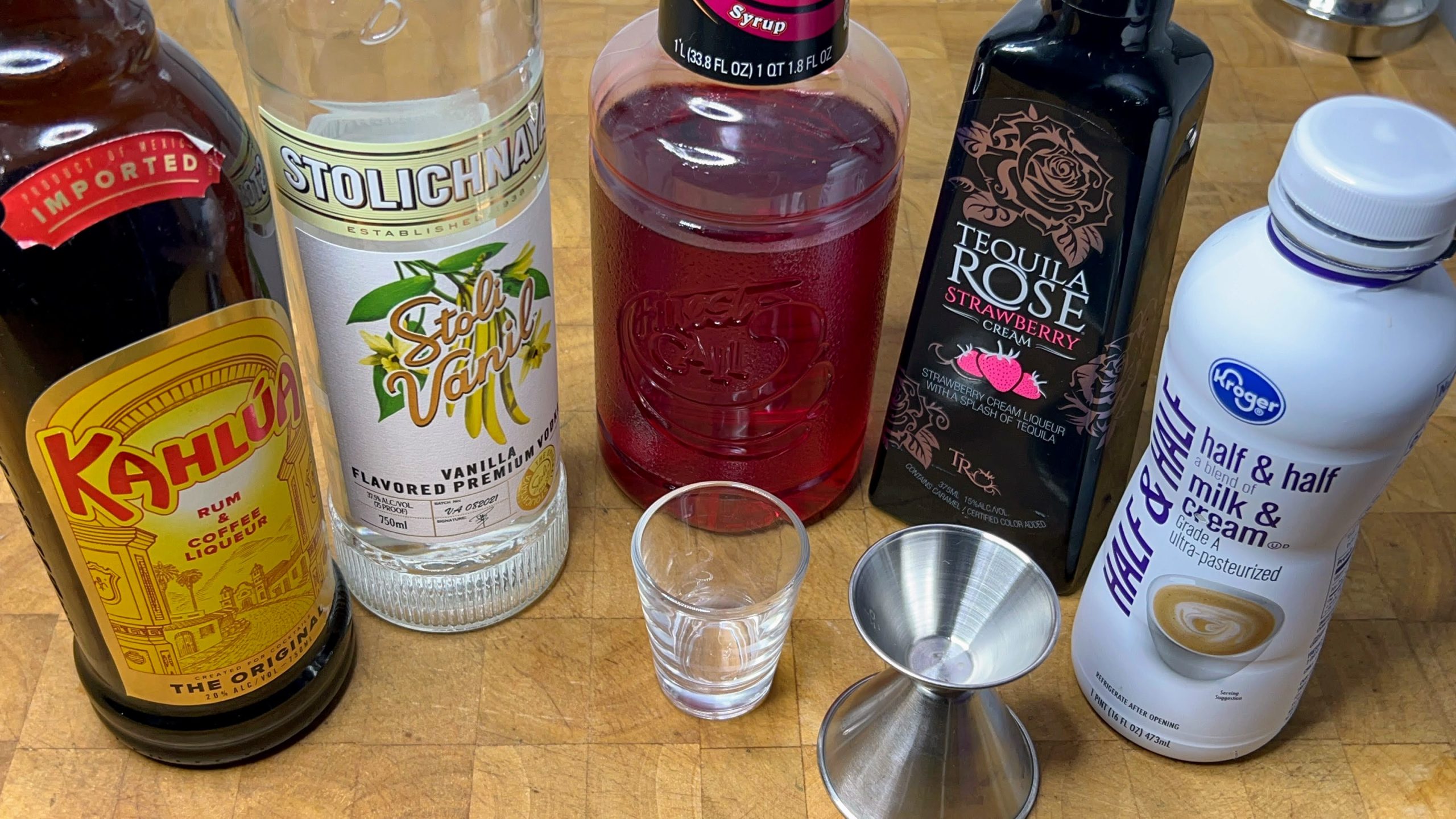 empty shot glass next to a jigger, kahlua, vanilla vodka, grenadine, tequila rose and half and half