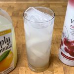 cherry vodka lemonade in a highball glass next to the ingredient bottles