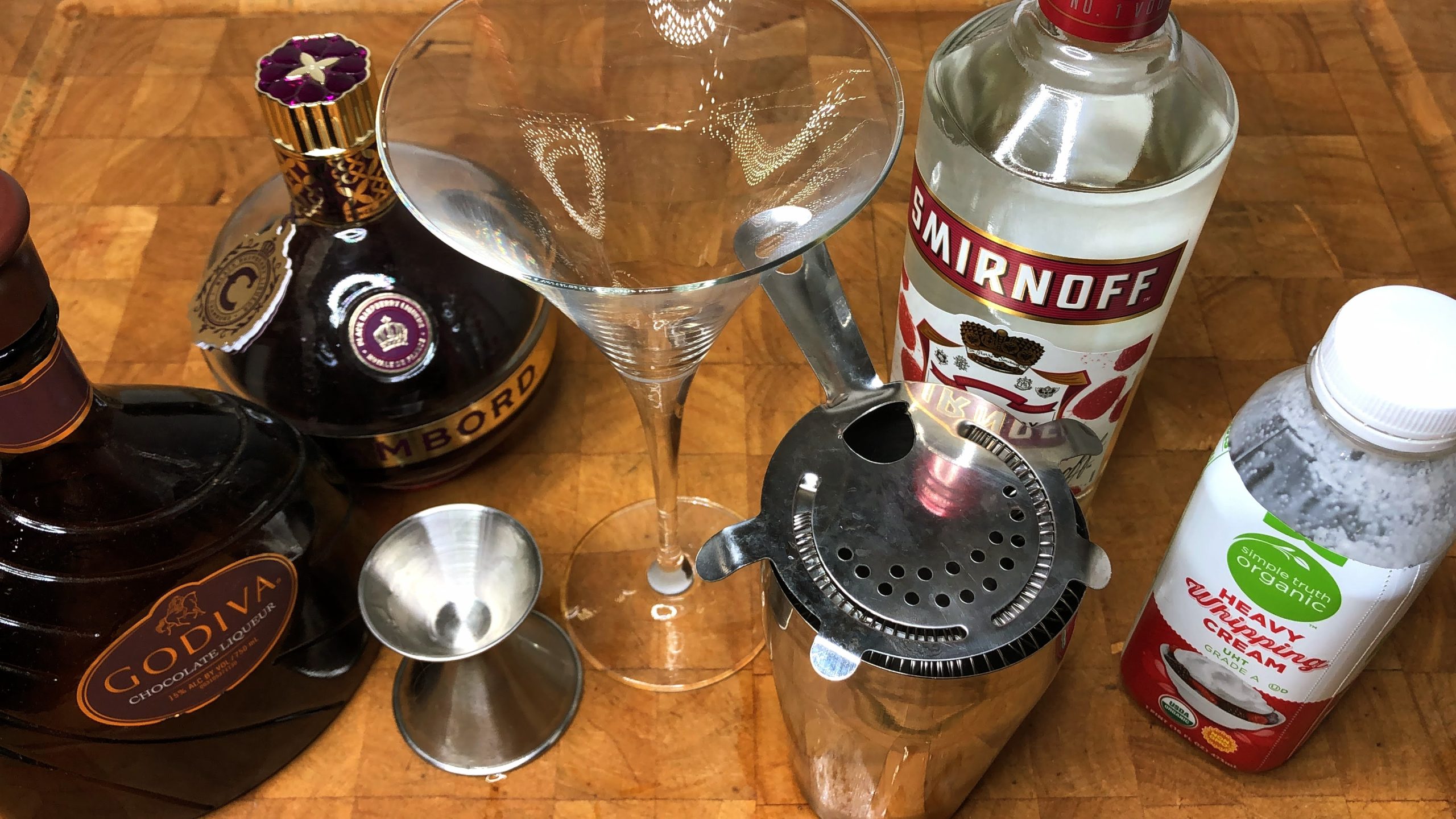 empty martini glass next to jigger, shaker, godiva liqueur, chambord, raspberrry vodka and heavy cream.