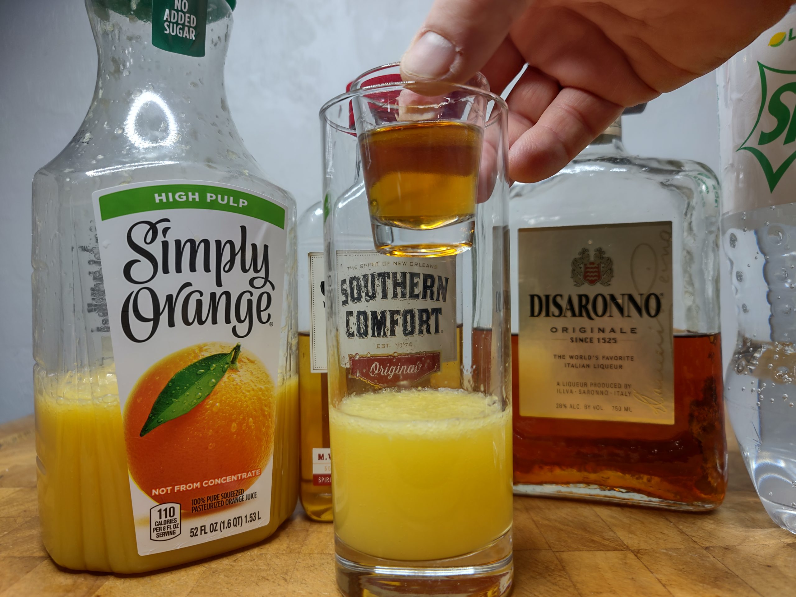 dropping a shot glass of soco and amaretto into a highball glass with OJ and sprite