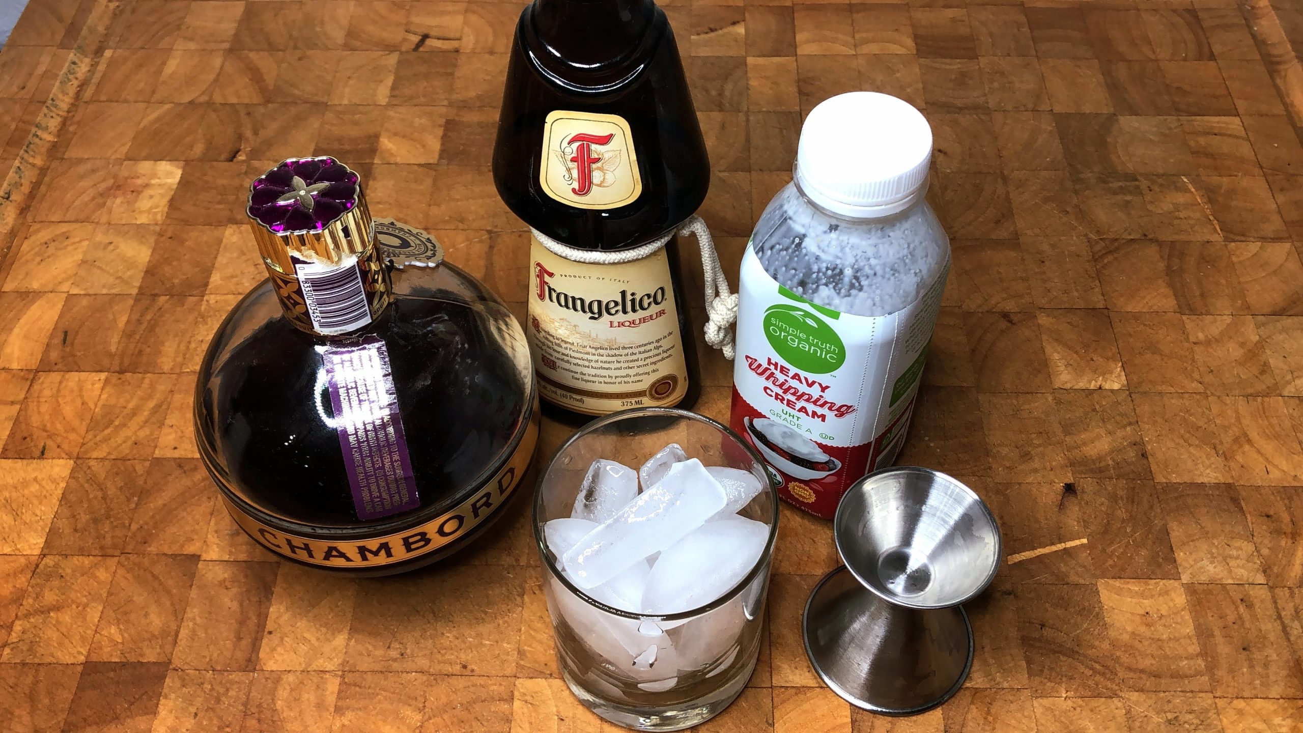 rocks glass filled with ice next to a jigger, heavy cream, frangelico and chambord