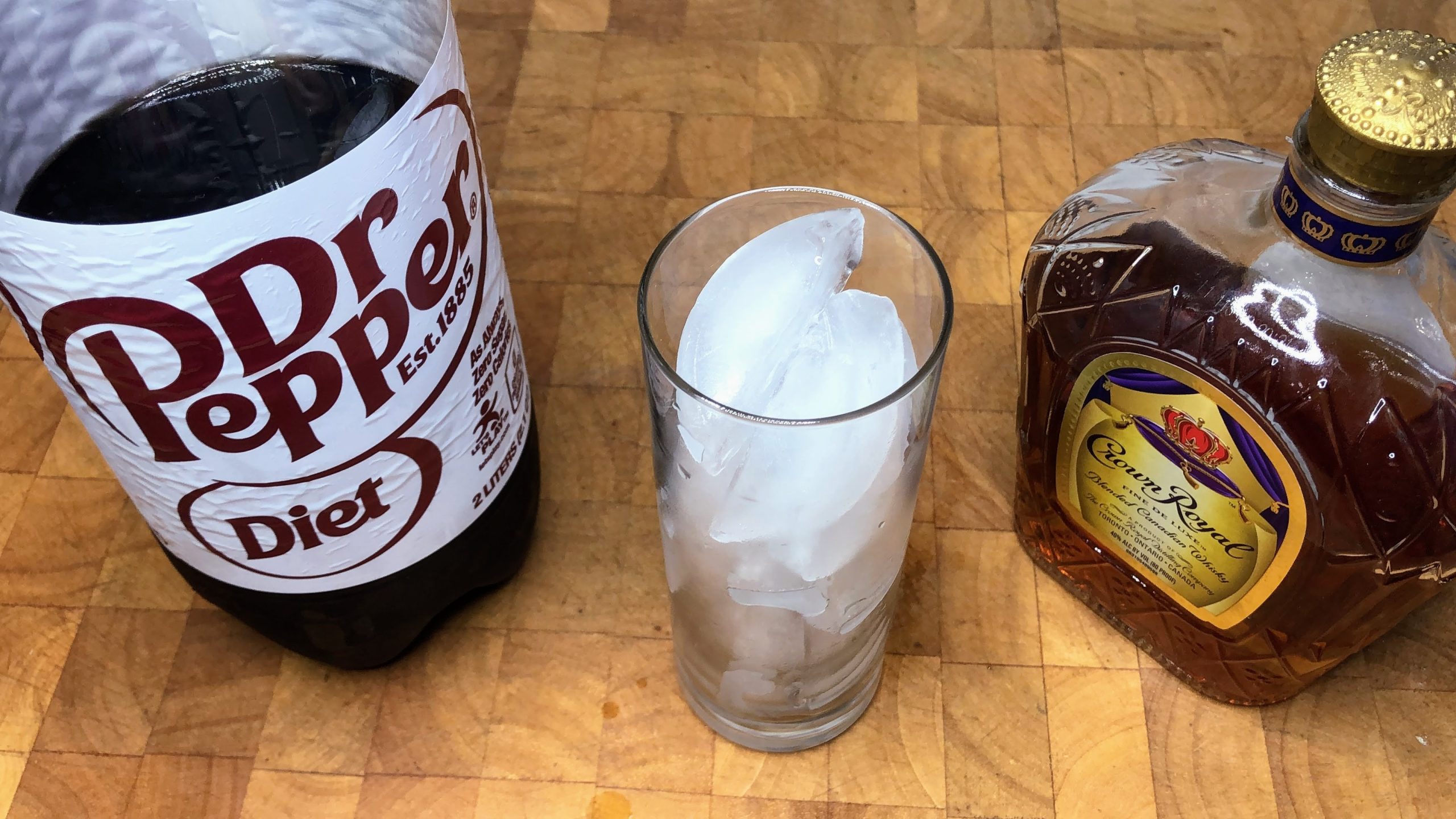 highball glass filled with ice next to bottles of crown royal and dr. pepper
