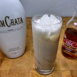 rumchata and cream soda in a highball glass surrounded by ingredient bottles