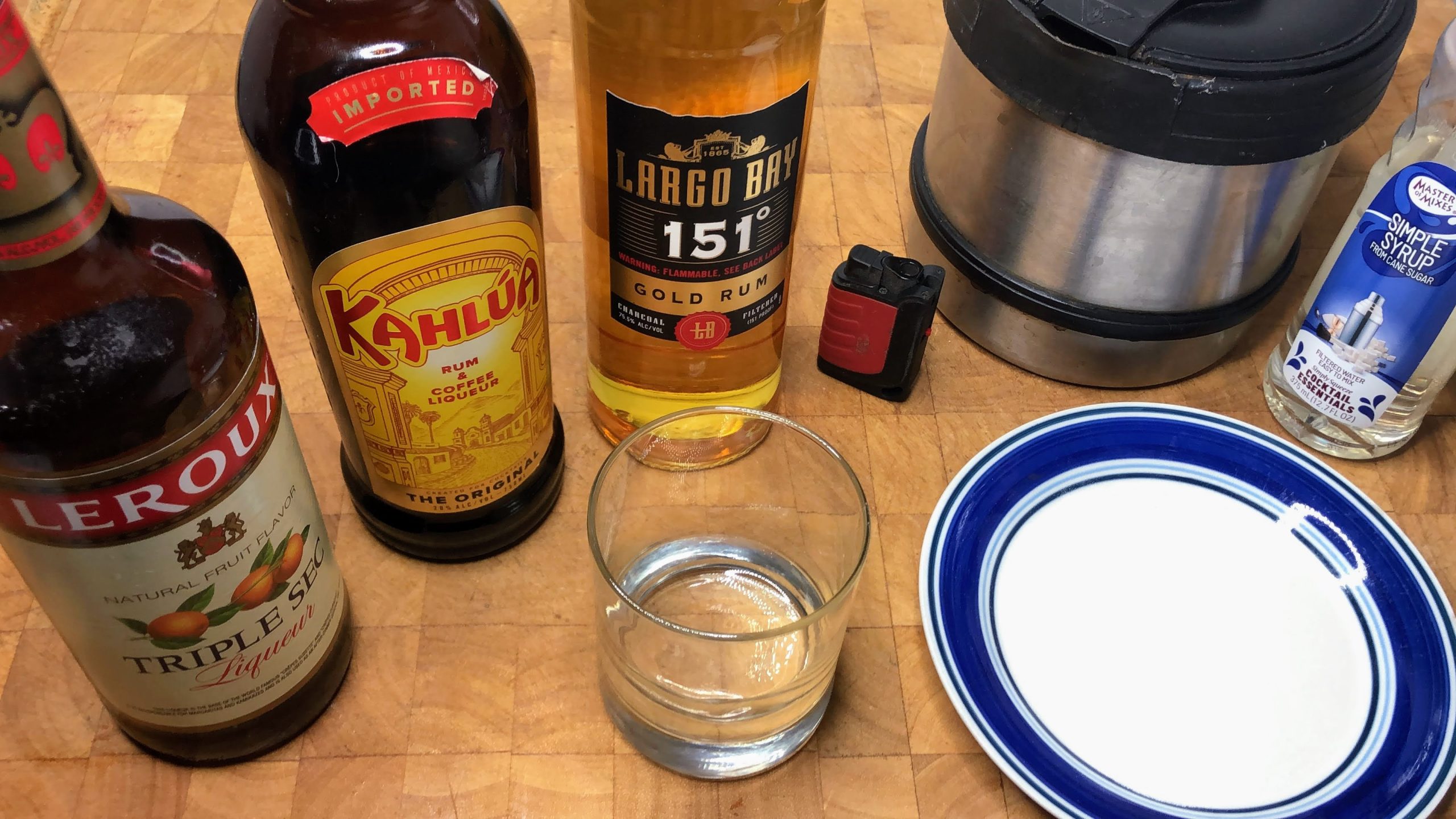 rocks glass next to saucer with sugar, simple syrup, coffee pot, lighter, 151 rum, kahlua and triple sec