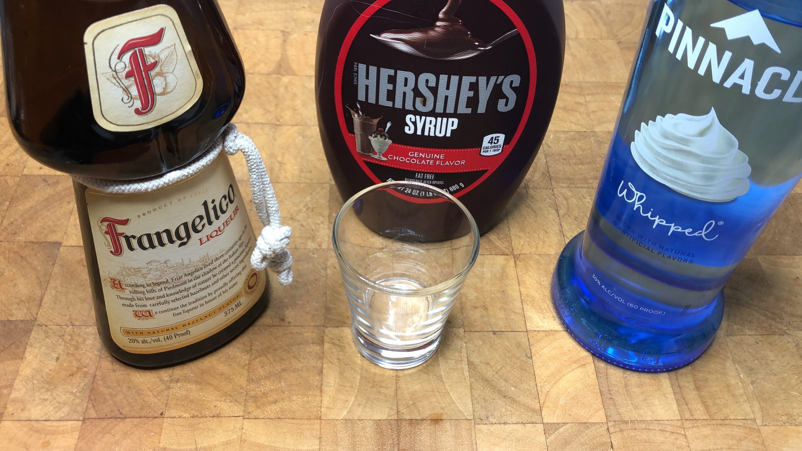 shot glass next to bottles of whipped cream vodka, frangelico and chocolate syrup