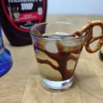 closeup of chocolate covered pretzel shot with ingredients next to the glass