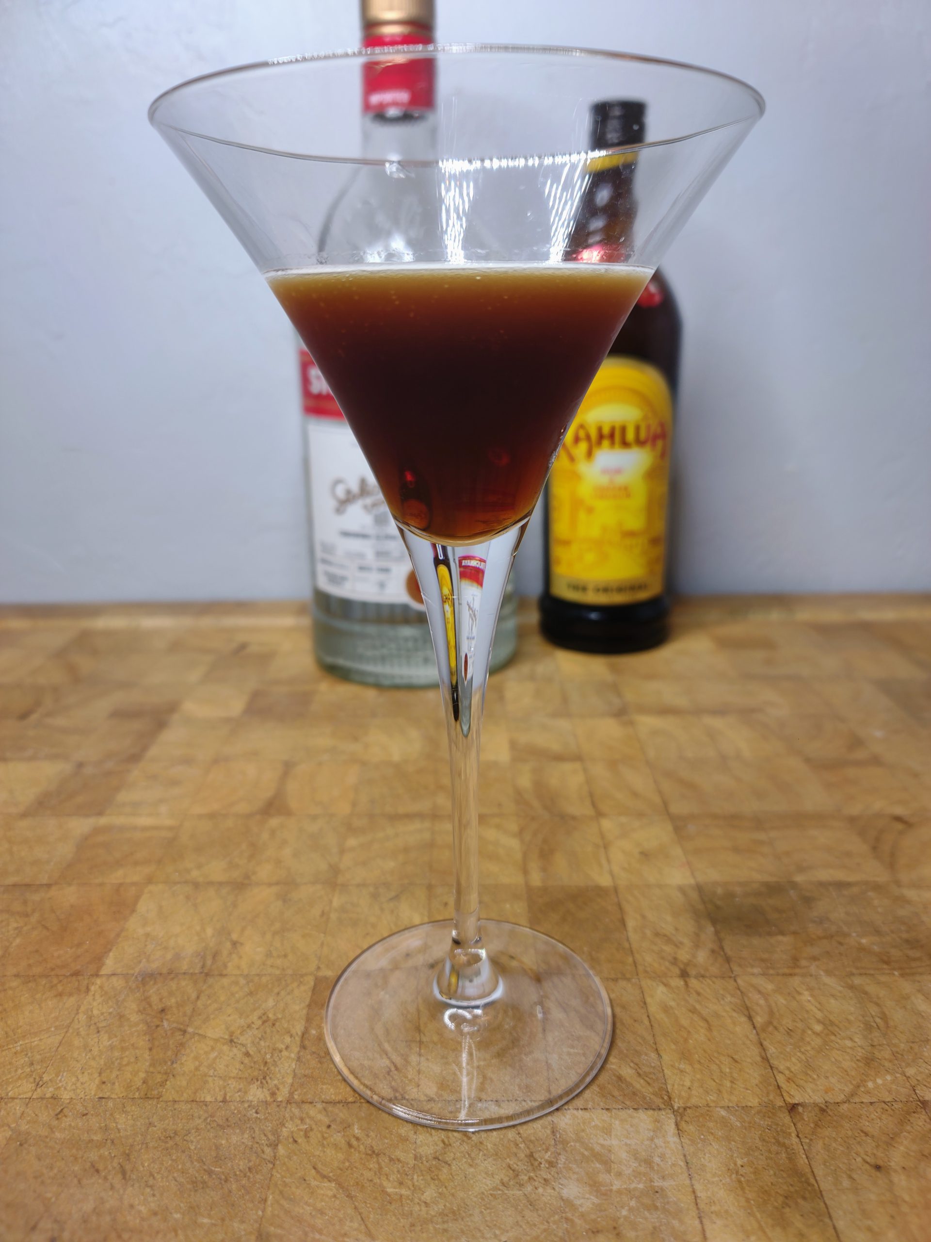 closeup of cold brew martini on a wooden table with ingredients behind the glass