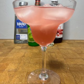 closeup of a cranberry margarita on a wooden table with ingredient bottles in the background