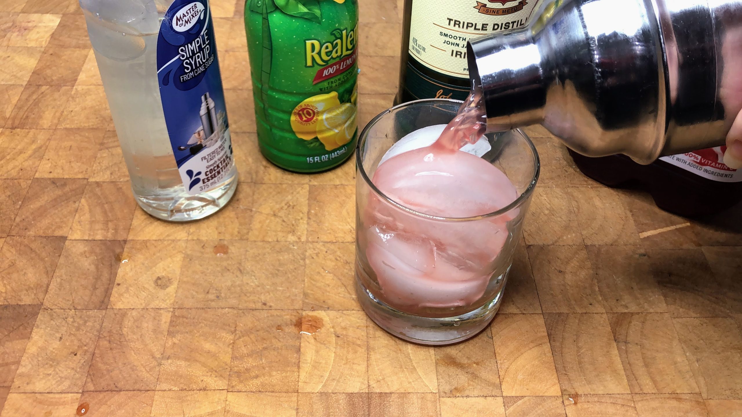 pouring cranberry whiskey sour into rocks glass