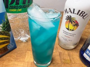 electric smurf drink in a highball glass with the ingredient bottles next to the glass.