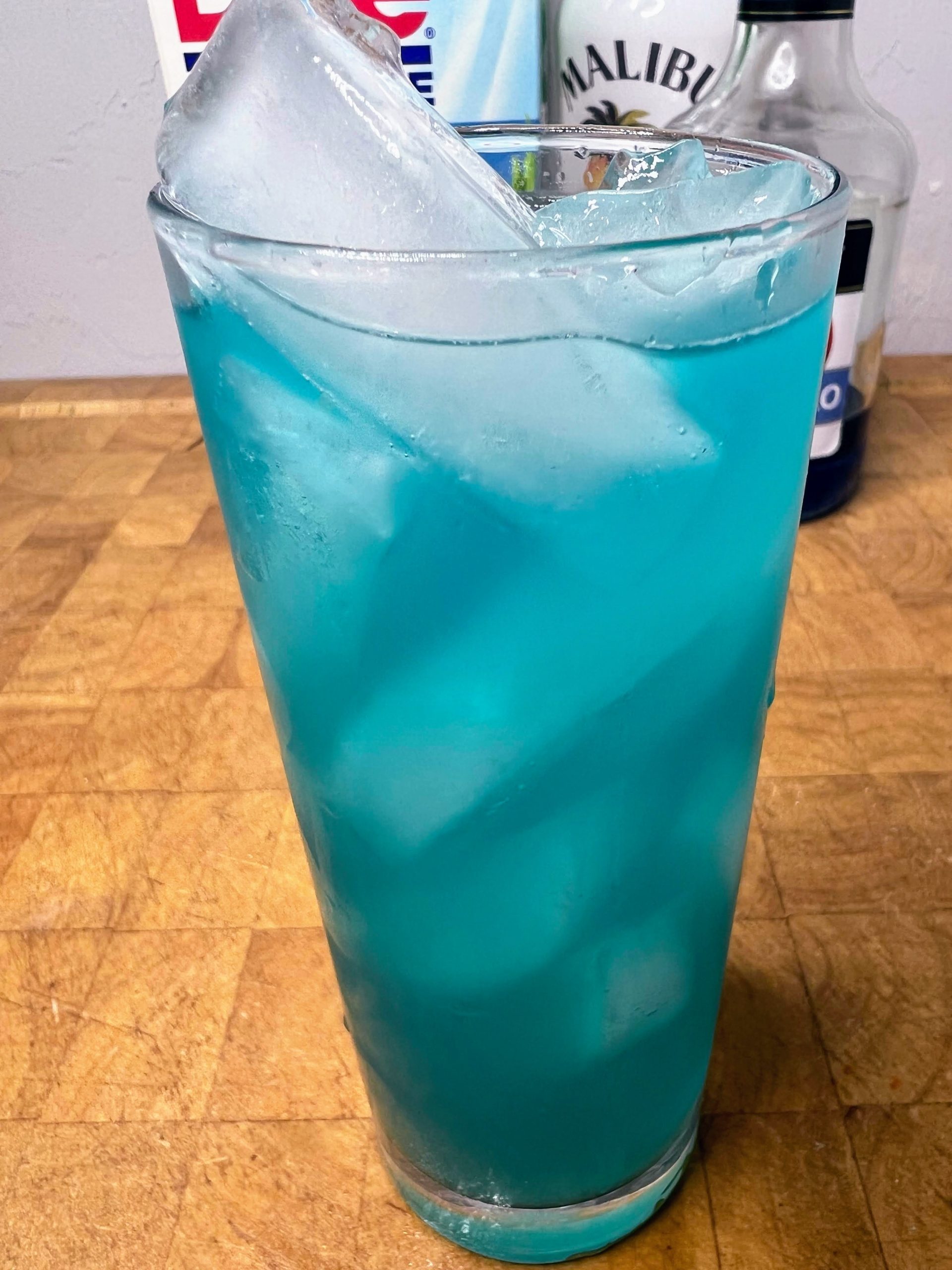 close up of electric smurf drink in a highball glass with ingredient bottles in the backgrund
