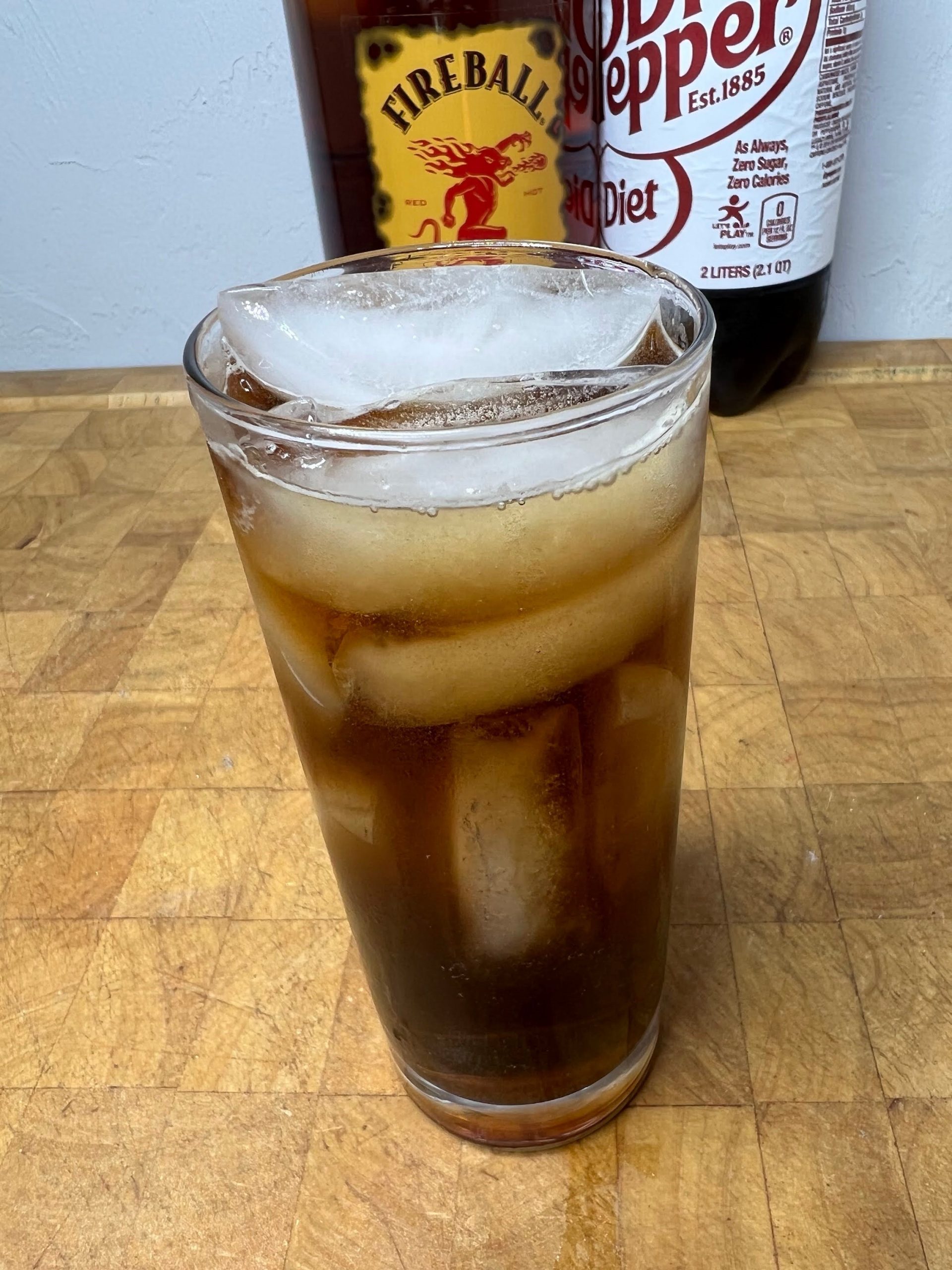 fireball and dr pepper in a highball glass with ingredient bottles behind the drink