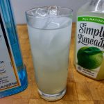 gin limeade in a highball glass with ingredient bottles next to the drink
