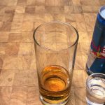 red bull in a highball glass next to shot glass of goldschlager and can of red bull