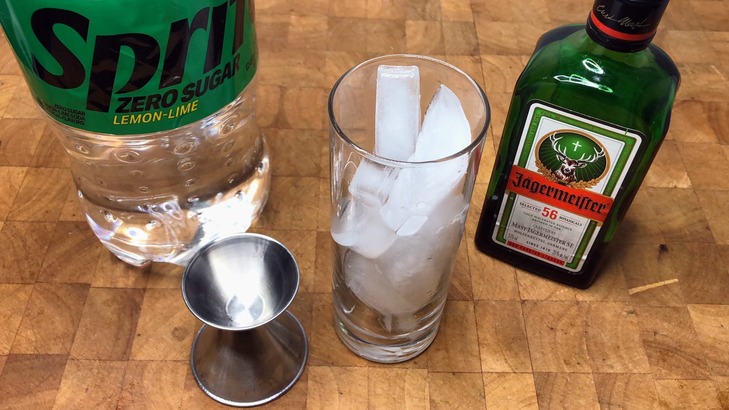 highball glass with ice next to jigger and bottles of jager and sprite