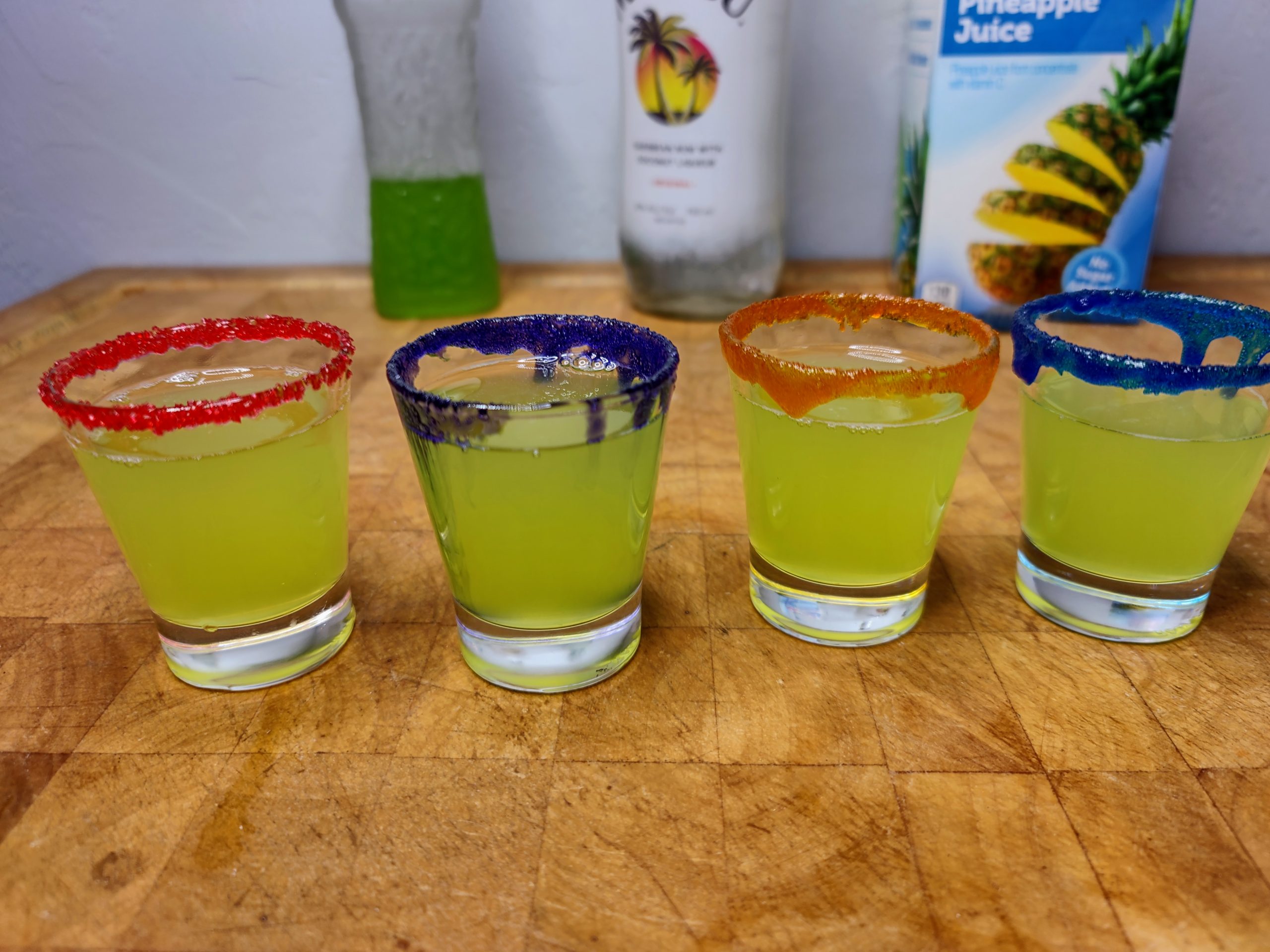 four ninja turtle shots lined up rimmed in red, purple, orange and blue with ingredients in the background