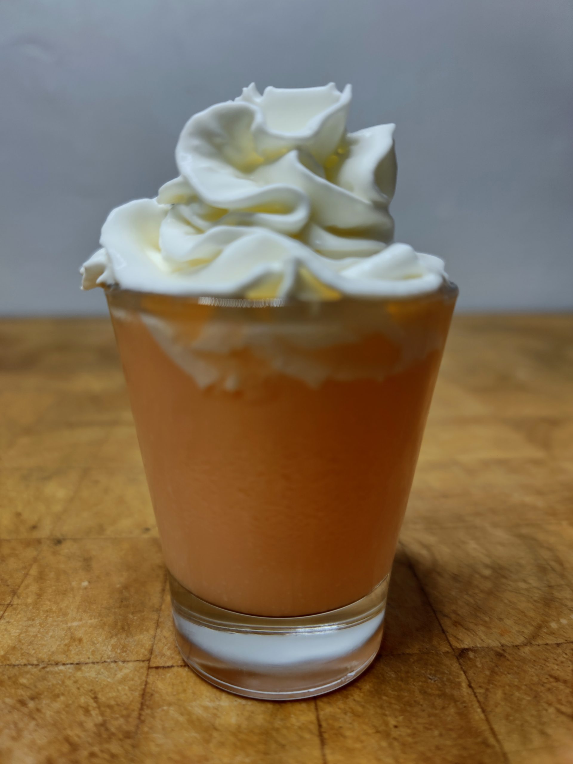 closeup of orange creamsicle shot topped with whipped cream on a wooden table